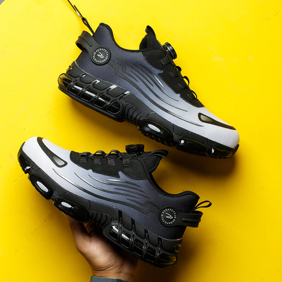 Black and gray work sneakers on a yellow background with a hand holding one shoe.